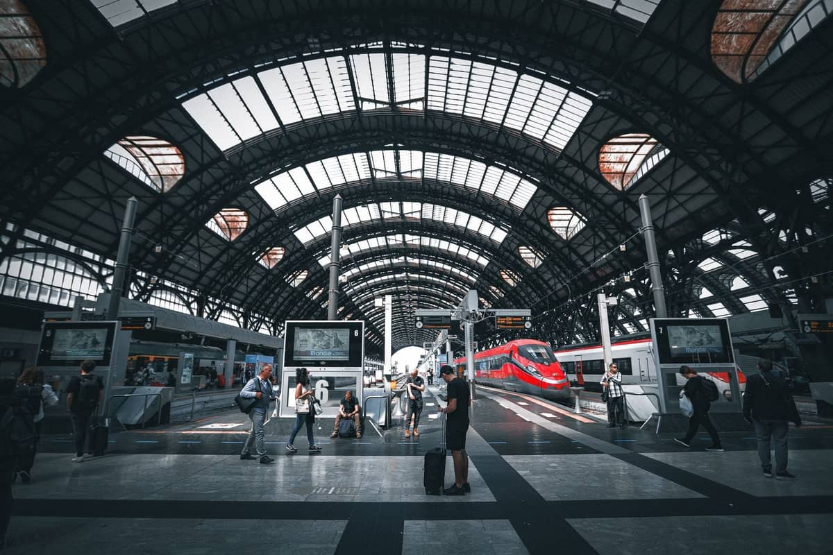 Cảnh nội thất ga Milano Centrale với hành khách, tàu cao tốc và cấu trúc mái vòm lớn ở phía sau.