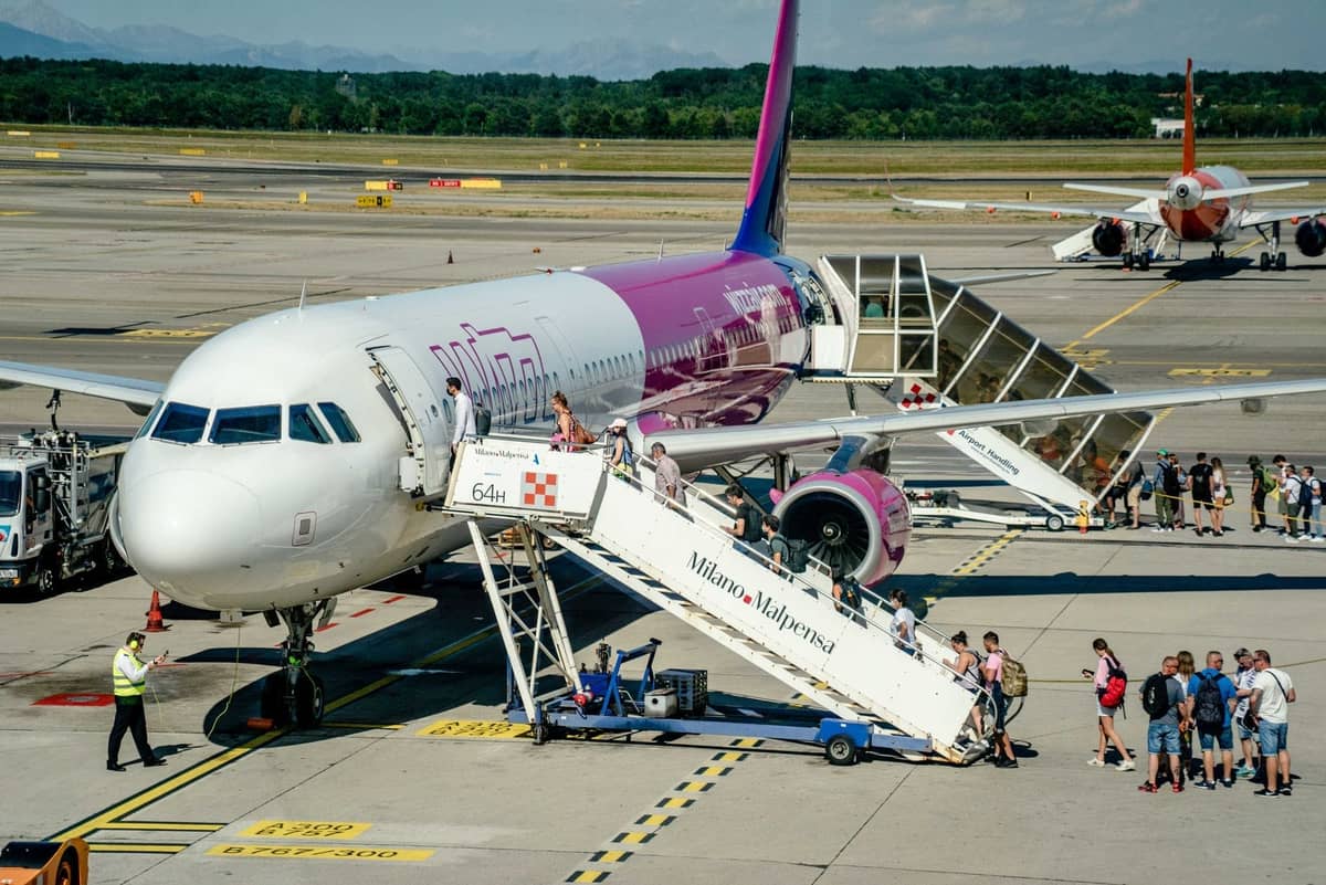 Hành khách lên máy bay qua cầu thang có ghi Milano Malpensa tại sân bay với người và máy bay hiện diện.