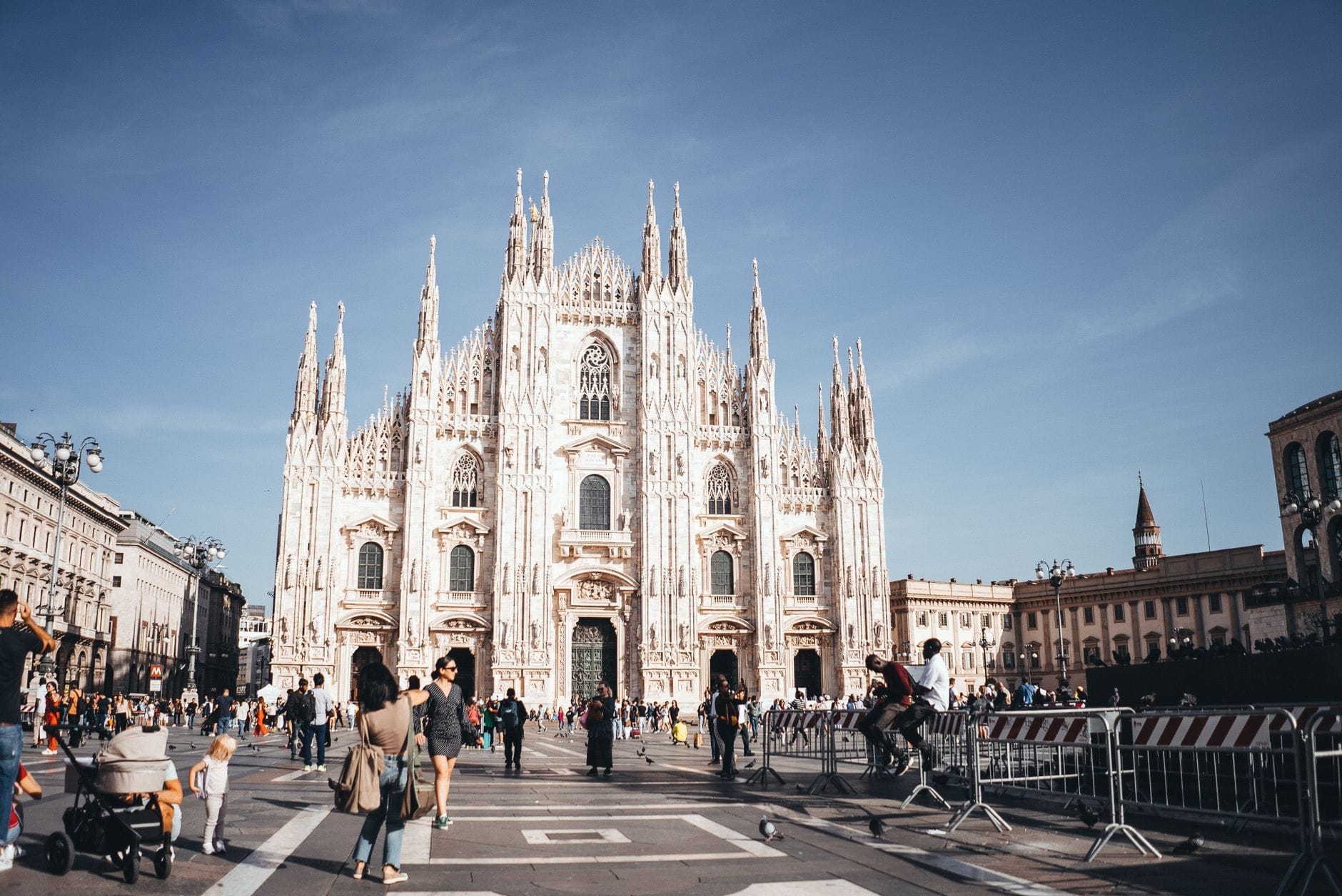 Piazza del Duomo movimentada em Milão com famílias, crianças em carrinhos e turistas caminhando em frente à catedral num dia ensolarado.
