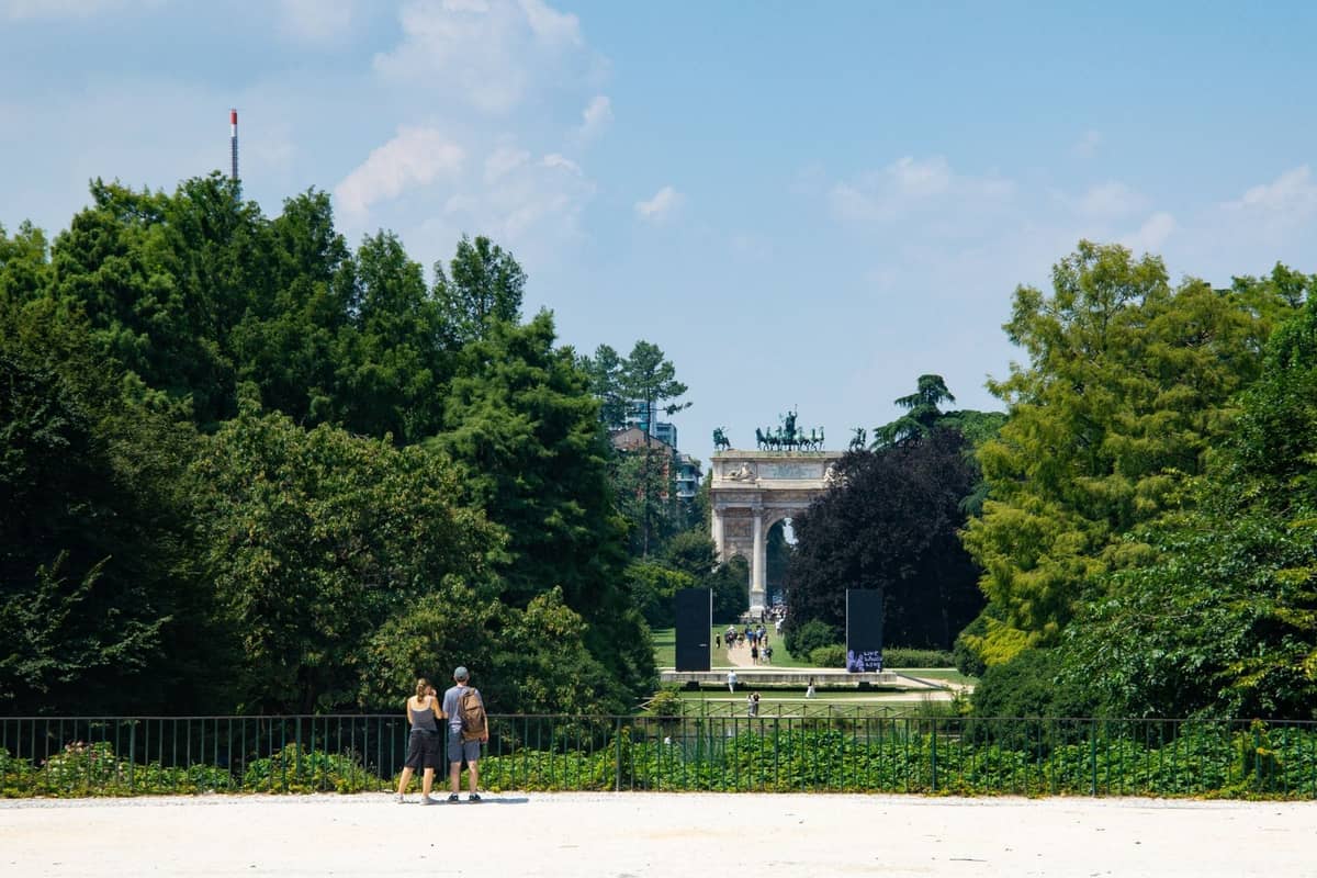Widok na Parco Sempione w Mediolanie z rodziną i Arco della Pace widocznym przez drzewa w słoneczny dzień.