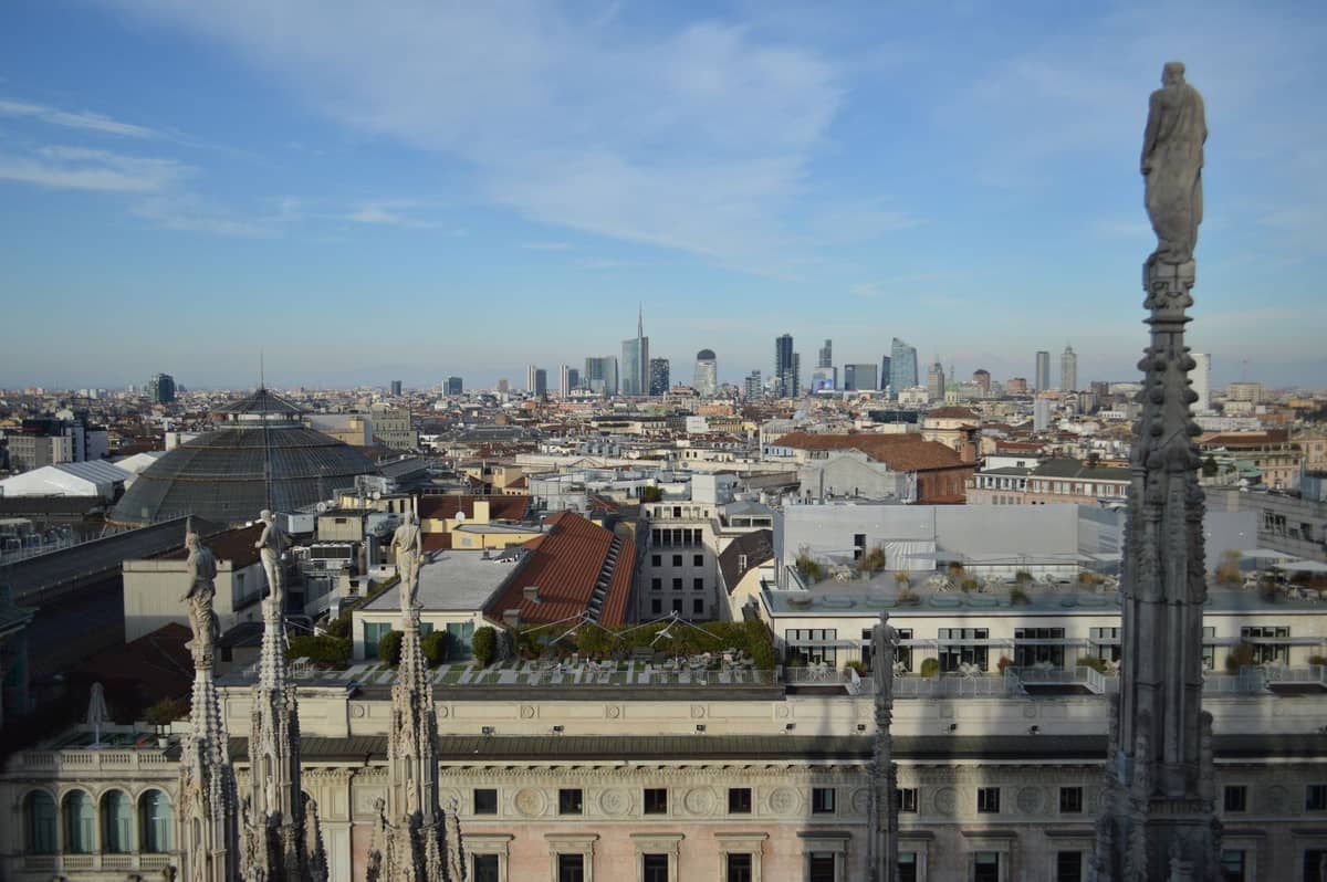 Słoneczny widok z dachu Duomo w Mediolanie z panoramą miasta i wieżyczkami katedry, ilustrujący przyjemną wiosenną pogodę i popularną atrakcję dla całej rodziny.
