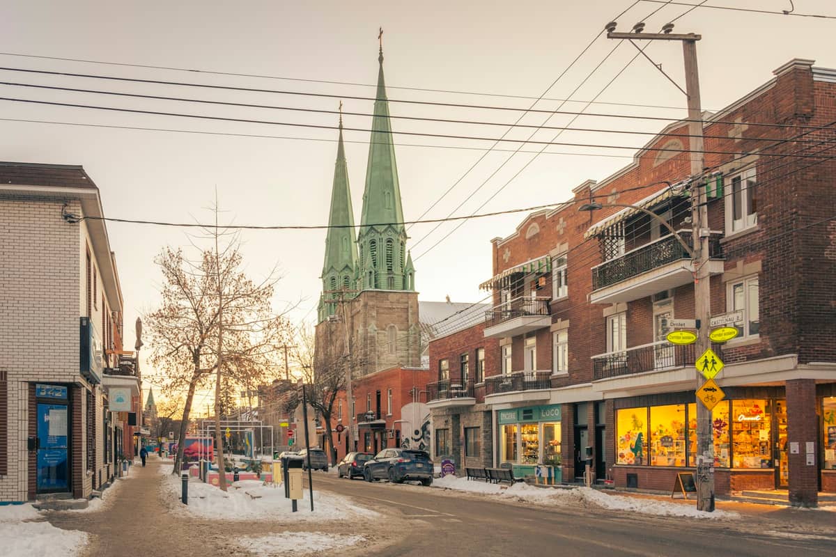 Straßenszene in Mile End mit kleinen Geschäften, Wohnhäusern und einer Kirche mit grünen Türmen an einem Wintertag