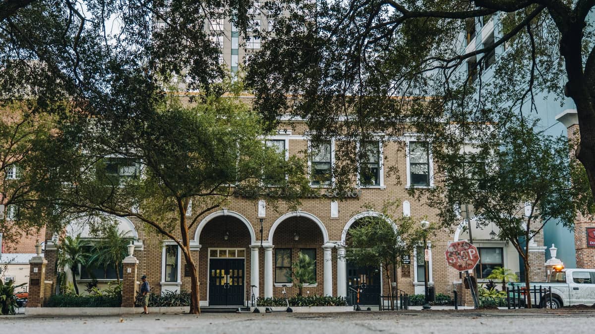 Straßenansicht eines Backsteingebäudes mit Bogenfenstern und alten Bäumen davor – typisch für das fußgängerfreundliche Viertelgefühl des Mills 50 District in Orlando.