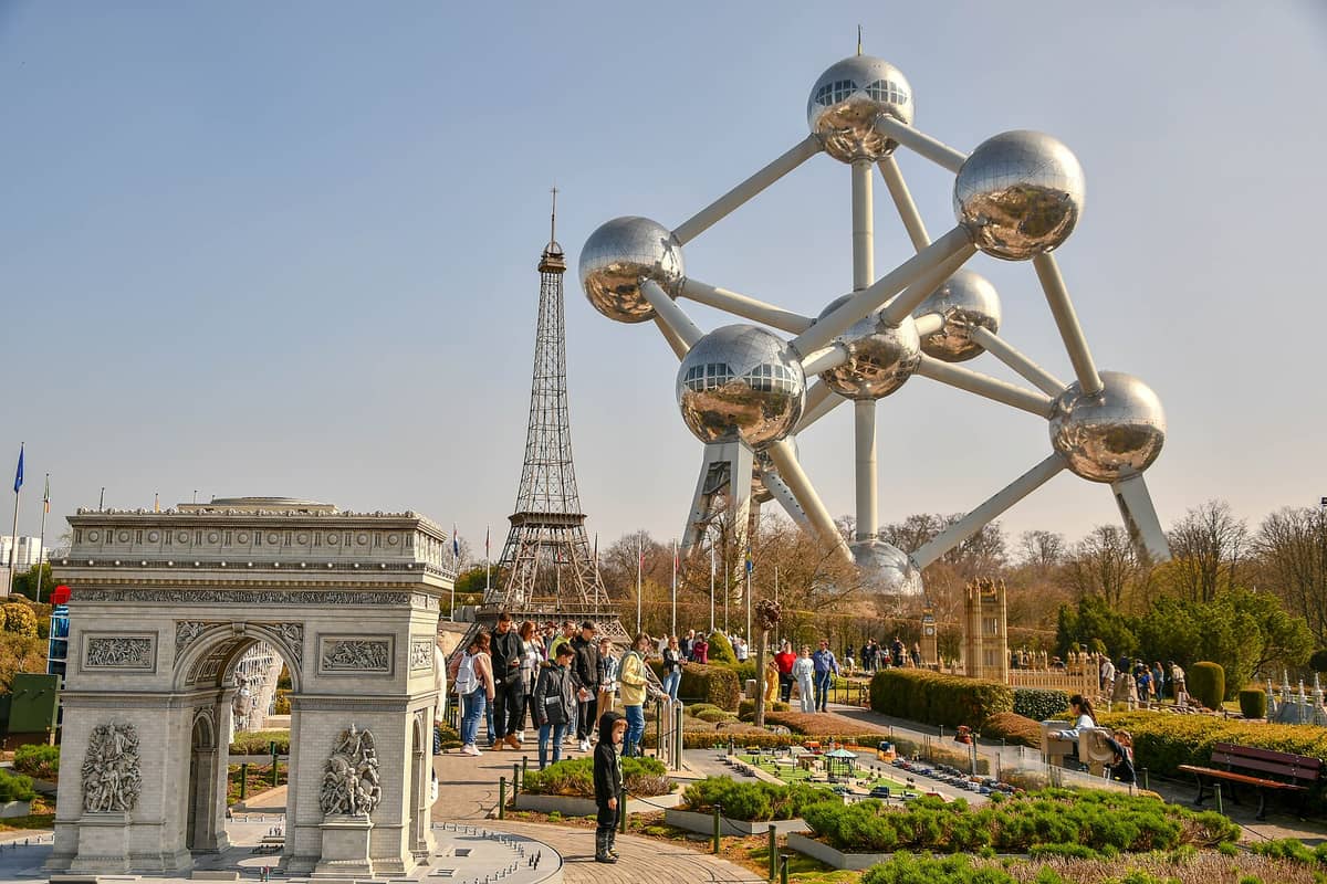O Mini-Europe em Bruxelas com visitantes caminhando entre maquetes detalhadas de monumentos europeus, incluindo o Arco do Triunfo e a Torre Eiffel, com o Atomium ao fundo.