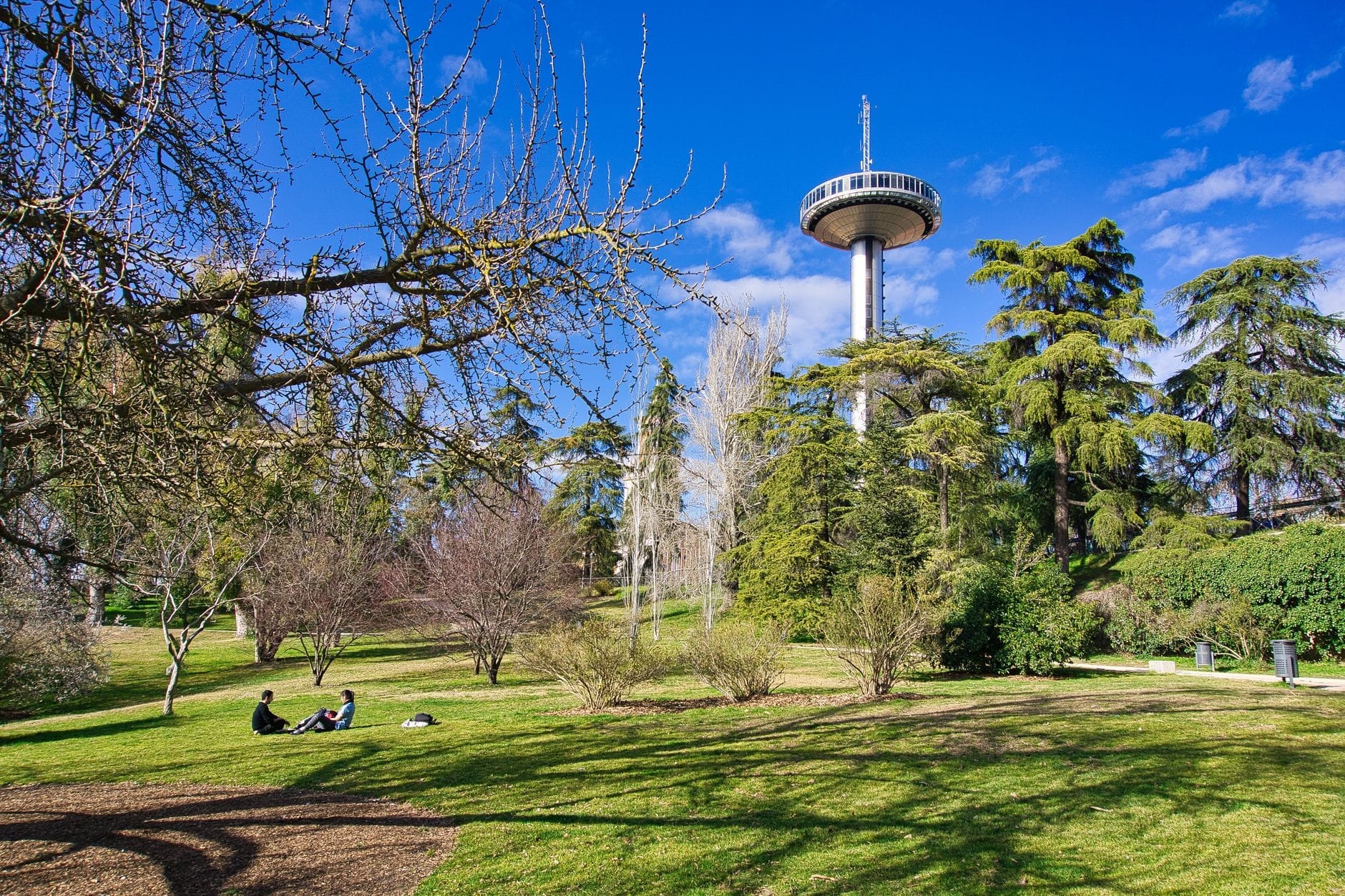 La torre belvedere del Faro de Moncloa si staglia su un parco rigoglioso, con persone che si rilassano sull'erba sotto un cielo azzurro intenso a Madrid.