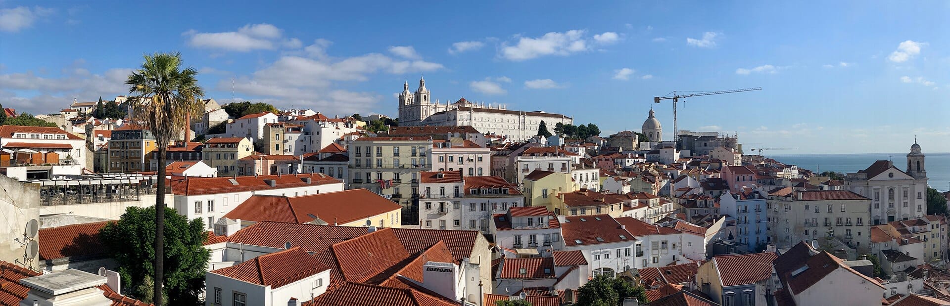 Vista panoramica dal Miradouro das Portas do Sol, con i tetti rossi di Alfama, la cupola bianca di São Vicente de Fora e il fiume Tago.