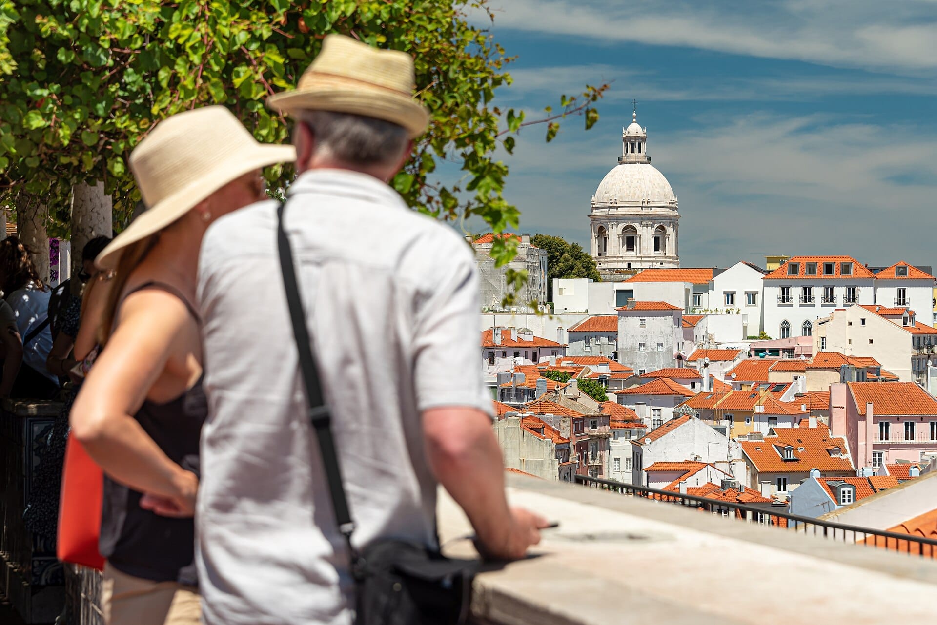 I visitatori al Miradouro de Santa Luzia osservano i tetti di tegole arancioni di Alfama e la cupola bianca del Panteão Nacional in una giornata di sole.