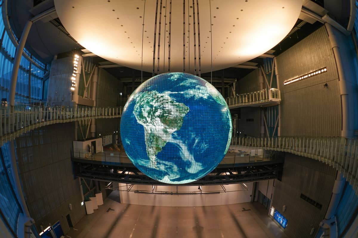 Interior of Miraikan with the large Geo-Cosmos globe exhibit suspended in a modern open hall, walkways and ambient lighting visible.