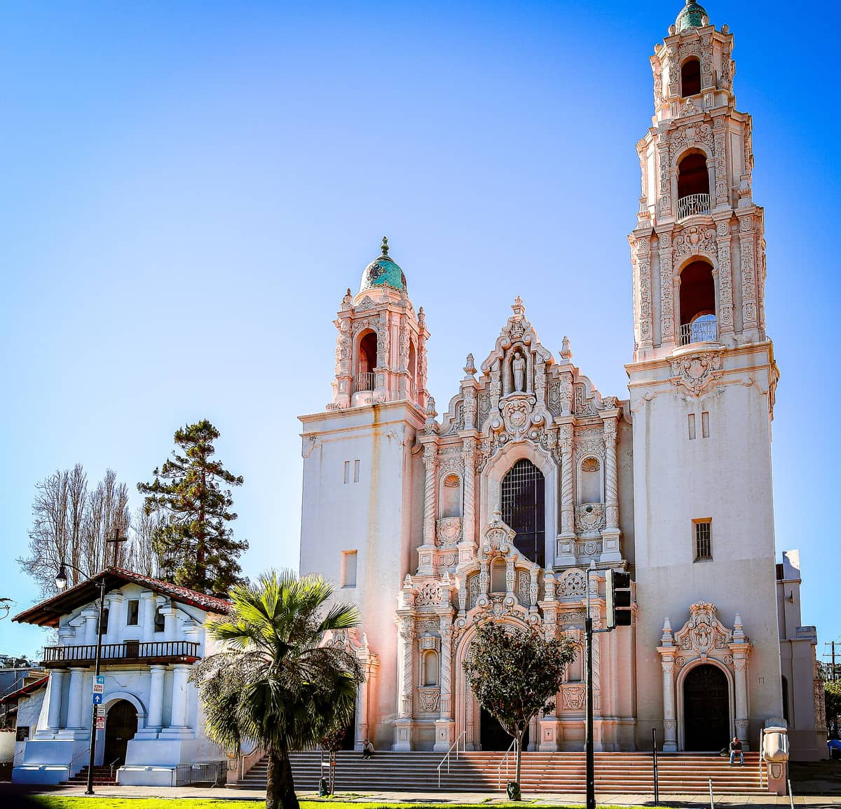 La Misión Dolores en San Francisco: a la izquierda, la blanca capilla de adobe; a la derecha, la ornamentada basílica con sus dos torres, bajo un cielo azul despejado.