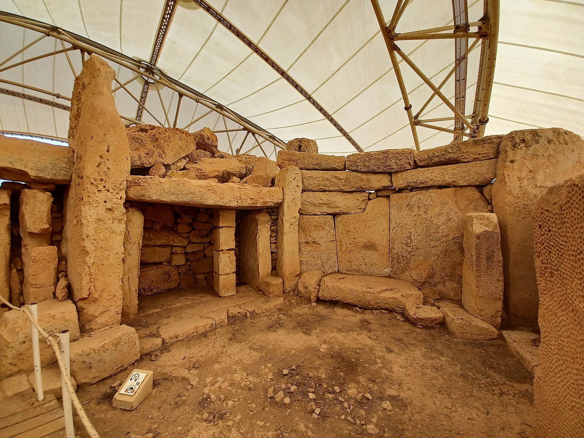 Vista interna dei Templi di Mnajdra con blocchi di calcare corallino e un antico portale in pietra sotto una tettoia protettiva a Malta.