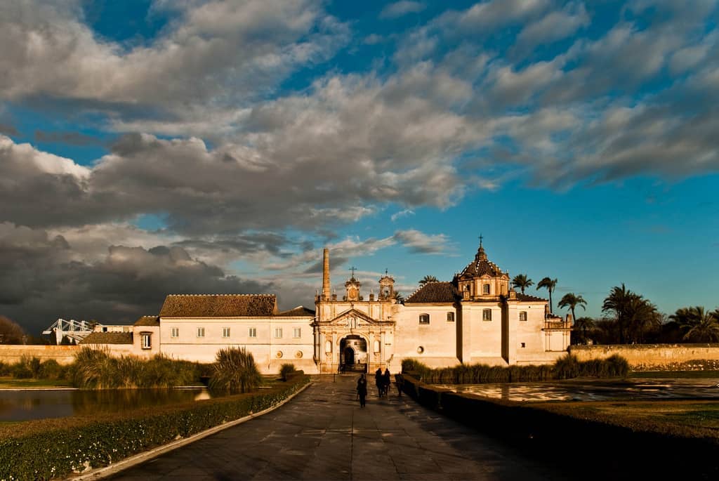 ด้านหน้าของ Monasterio de la Cartuja ในเมือง Seville พร้อมเมฆที่สวยงามน่าตื่นตาและแสงแดดอบอุ่นส่องสว่างตัวอาคารอารามประวัติศาสตร์