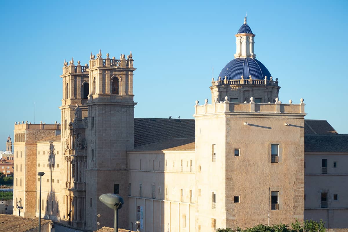 Vista esterna del Monasterio de San Miguel de los Reyes a Valencia, con le torri caratteristiche e la cupola piastrellata di blu sotto un cielo sereno.
