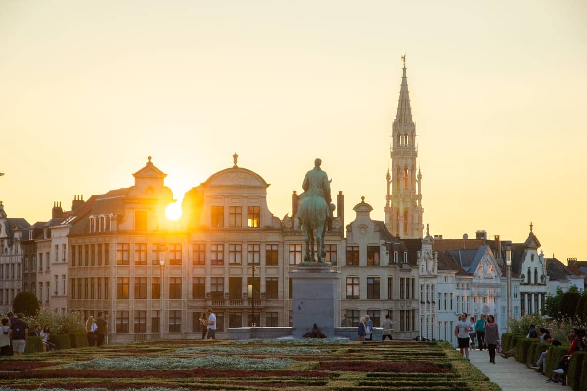 Vista ao pôr do sol do Mont des Arts em Bruxelas, mostrando os jardins em terraços, uma estátua equestre e o campanário da Câmara Municipal ao fundo.