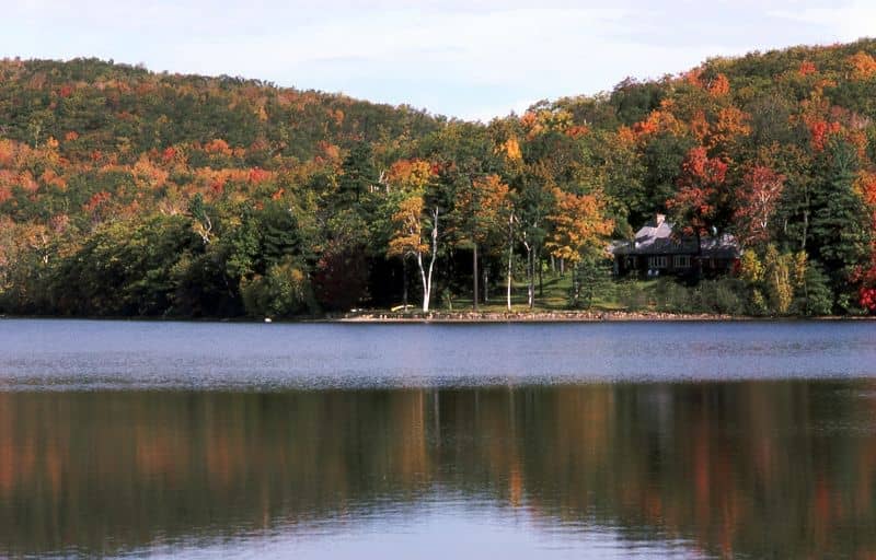 Blick auf einen ruhigen See, umgeben von bunten Herbstwäldern und einer Hütte im Mont-Saint-Bruno-Nationalpark bei Montreal.
