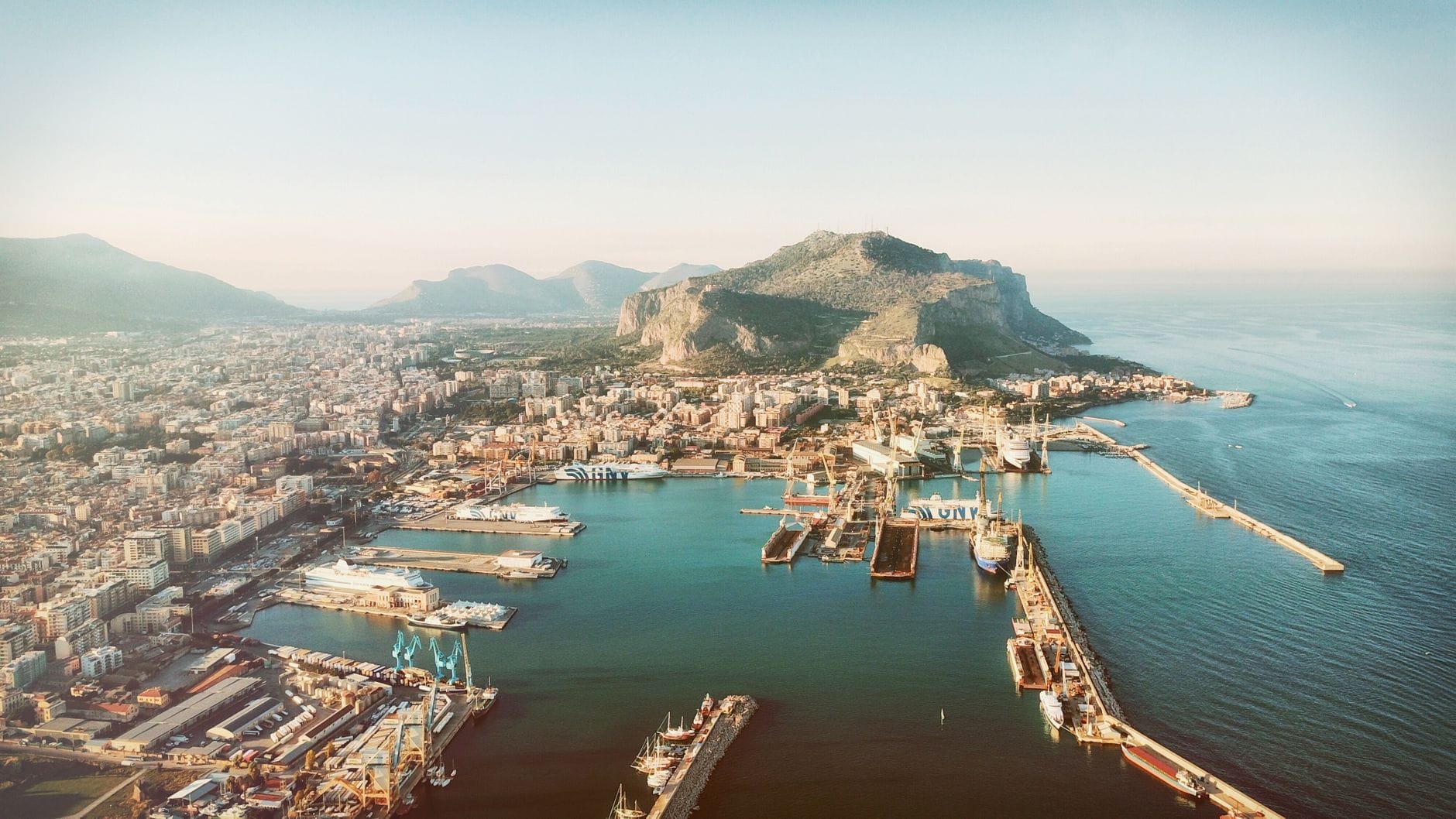 Luftaufnahme von Palermo mit dem Monte Pellegrino, der sich über die Stadt und den Hafen erhebt – Berg und Stadtlandschaft unter klarem Himmel.
