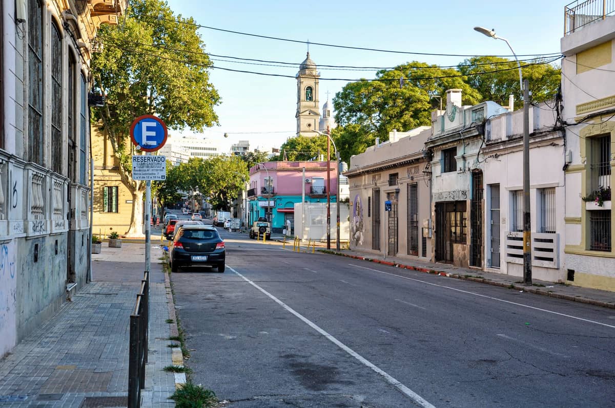ถนนเงียบสงบในย่านประวัติศาสตร์ของ Montevideo พร้อมอาคารเตี้ย รถยนต์จอดอยู่ และยอดโบสถ์ในระยะไกล