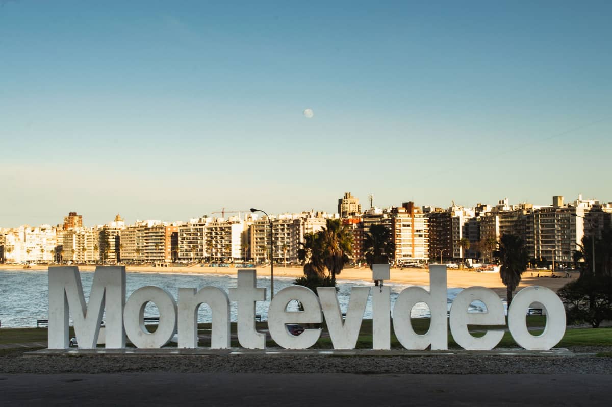 ป้าย Montevideo สีขาวขนาดใหญ่ริมชายหาด Rambla และฉากหลังเป็นตัวเมืองใต้ฟ้าใสและน้ำทะเล ในเมืองหลวงอุรุกวัย