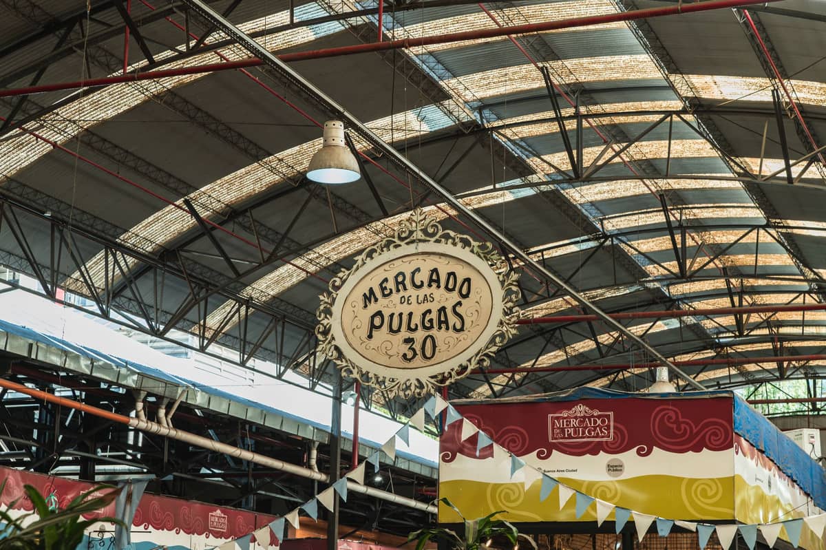 มุมมองกว้างของตลาดนัดในร่ม Mercado de las Pulgas ในมอนเตวิเดโอ พร้อมป้ายที่โดดเด่นและธงประดับตกแต่งใต้หลังคาโค้ง