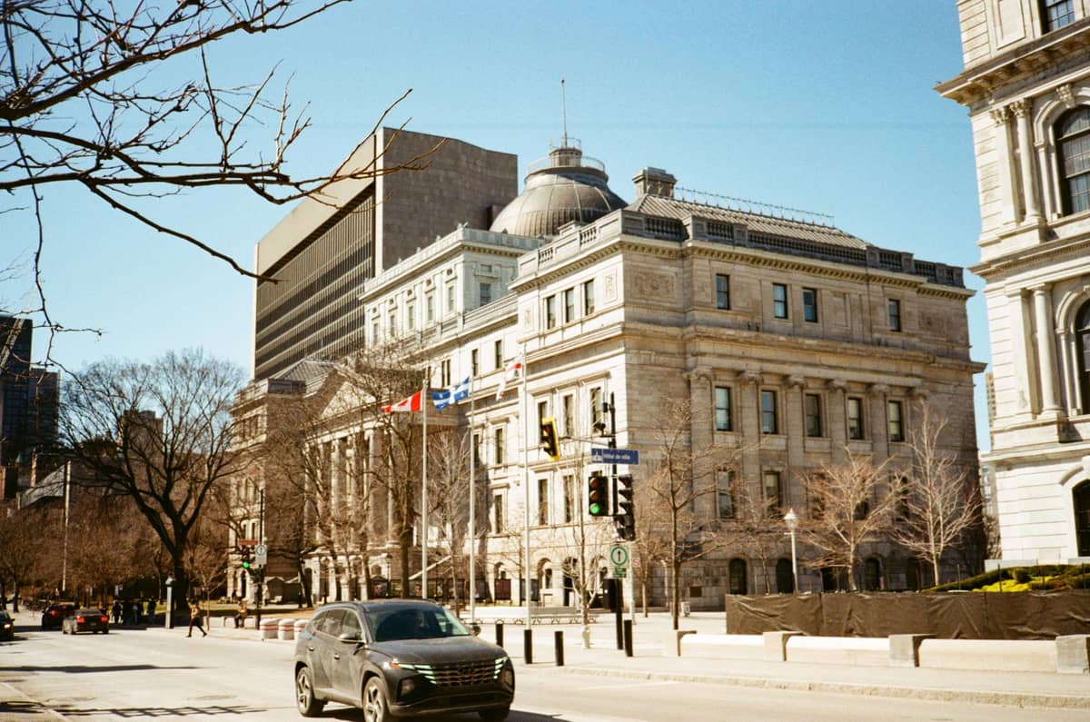 Stone institutional building with dome and flags along a downtown Montreal street on a sunny day