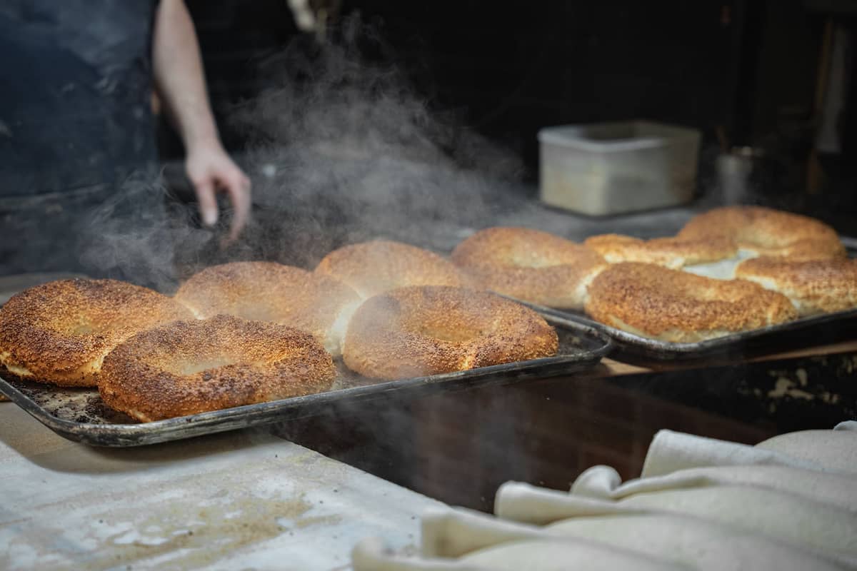 Frisch gebackene Montrealer Bagels mit Sesamsamen, dampfend auf Backblechen in einer traditionellen Bagel-Bäckerei.