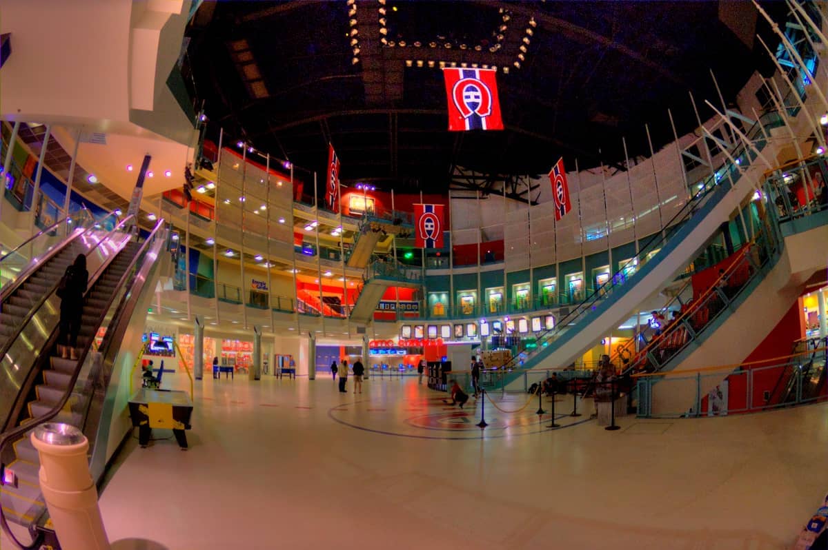Weitläufiger Blick in das Innere des Montreal Forum mit großen Bannern, Rolltreppen, moderner Architektur und Besuchern, die die mehrstöckige Arena erkunden.