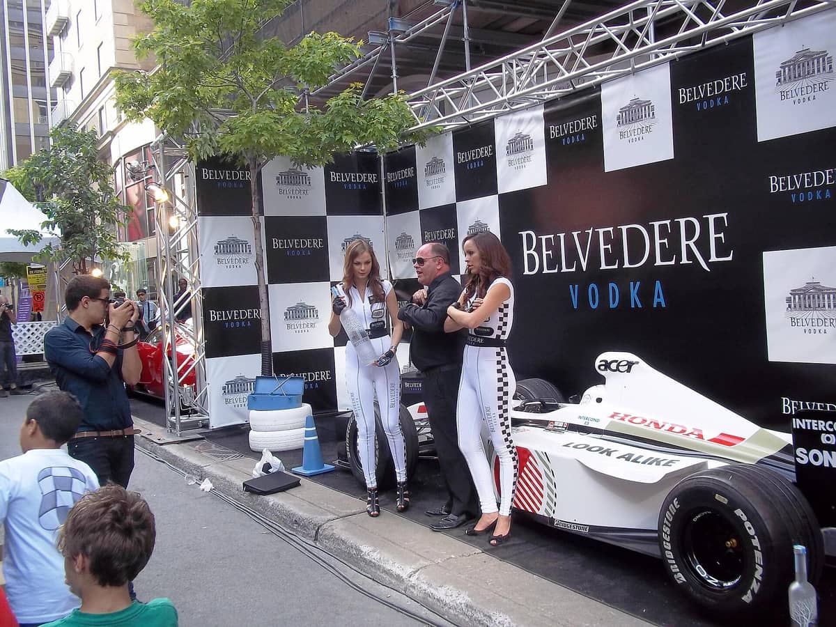 Straßenszene während des Grand Prix de Montreal-Wochenendes auf der Crescent Street, mit Personen, die neben einem Showcar vor Sponsorenbannern posieren.
