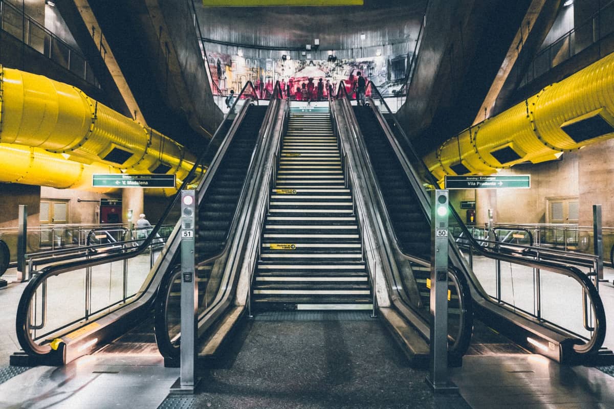 Weitwinkelansicht des Rolltreppenzugangs in der Metrostation Jean-Drapeau in Montreal mit markanten gelben Rohren und Beschilderung.