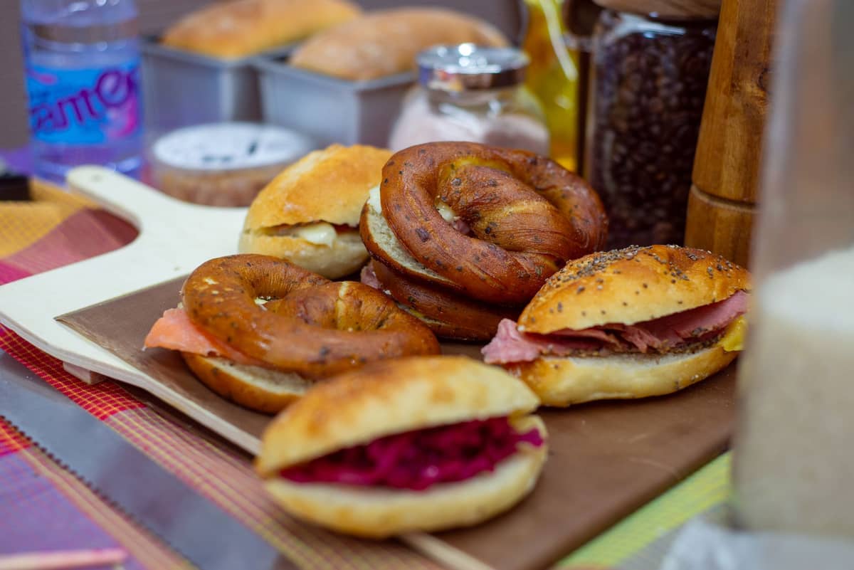 Verschiedene Bagels und Sandwiches im Montreal-Stil auf einem Schneidebrett angerichtet, mit Delikatessen-Zutaten im Hintergrund.