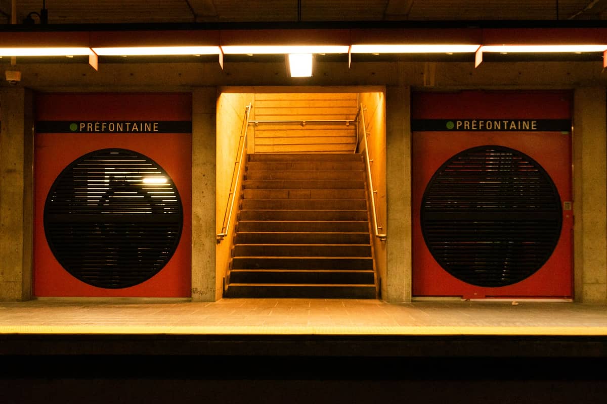 Bahnsteig der Station Prefontaine der Métro Montreal mit markanten runden schwarzen Gittertüren und orange-roten Akzenten, Treppe zum Ausgang in der Mitte.