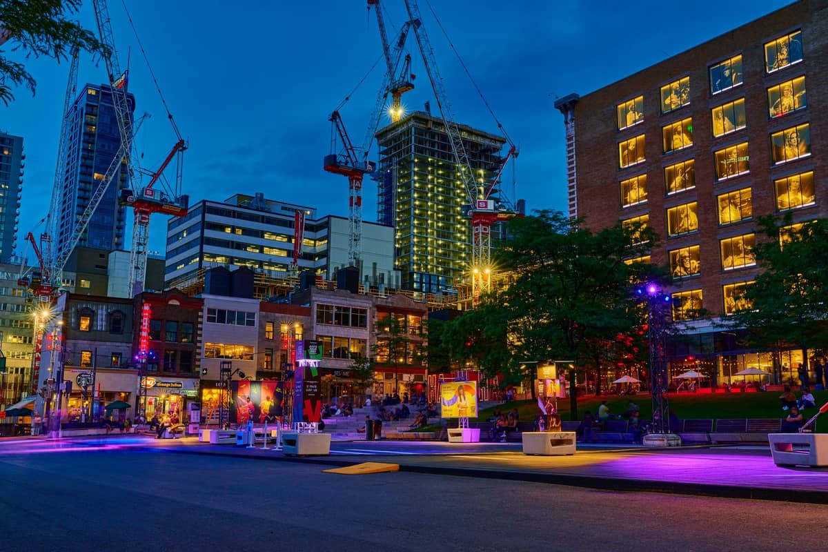 Der Quartier des Spectacles in Montreal in der Abenddämmerung, mit lebhafter Festivalbeleuchtung, Menschen und modernen Gebäuden im Hintergrund während einer Veranstaltungsnacht.