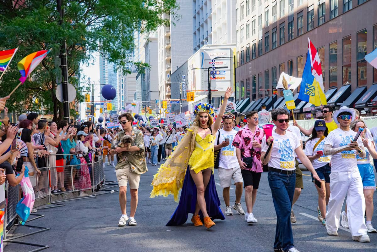 ขบวนพาเหรด Pride อันสดใสบนถนนในเมือง นำโดยนักแสดงดรากในชุดสีเหลือง ท่ามกลางฝูงชนจำนวนมาก ธงสีรุ้ง และฉากหลังเมืองสไตล์ Montréal