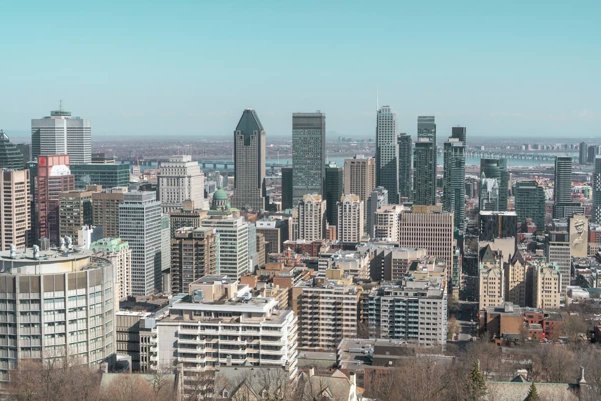 Montreal city skyline viewed from above during daytime, featuring Mont Royal, landmark skyscrapers, and clear blue sky.