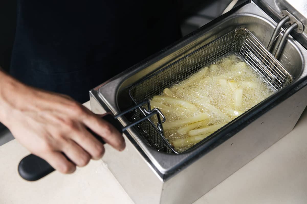 Nahaufnahme von dickgeschnittenen Pommes frites, die in einem Frittierkorb mit sprudelndem Öl frittiert werden, mit Fokus auf die Textur der Pommes.