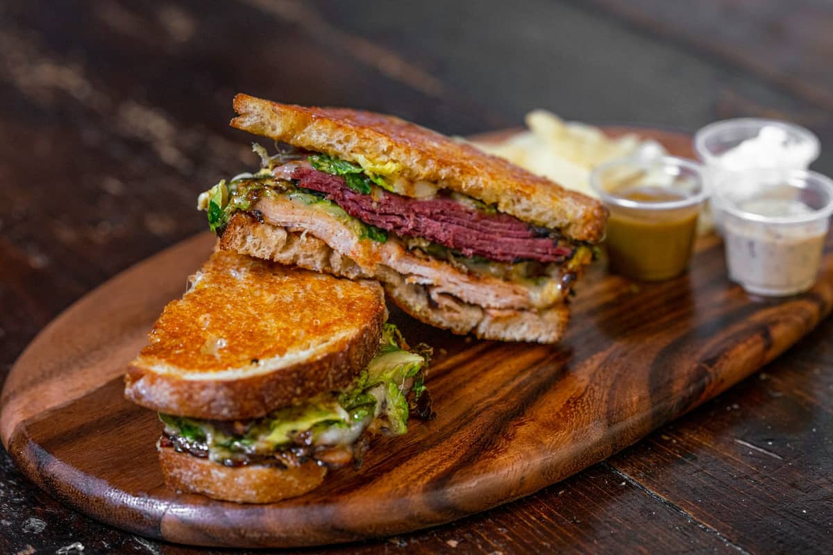 Un classico sandwich di carne affumicata di Montreal su pane di segale, ripieno di strati di manzo stagionato rosato, servito su un tagliere di legno con senape.