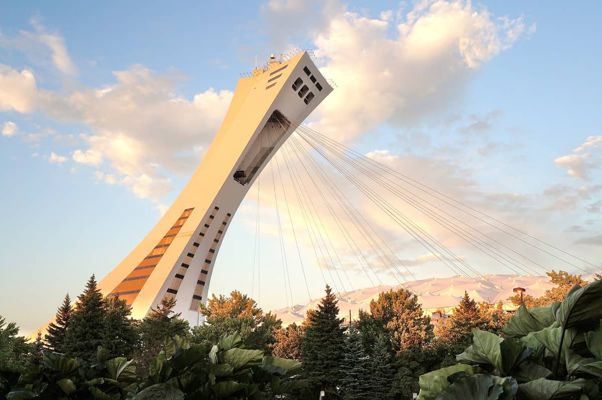 Der Montreal Tower im Olympiapark mit seiner markant geneigten Konstruktion und den Stahlseilen, eingerahmt von Bäumen und einem pastellfarbenen Abendhimmel.