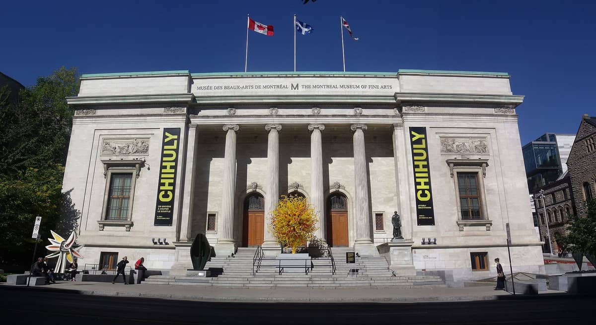 Fasada Montreal Museum of Fine Arts z klasycznymi kolumnami, rzeźbami i flagami nad wejściem w słoneczny dzień.