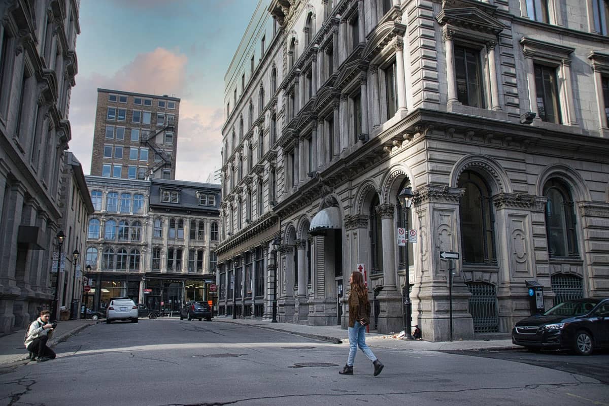 Eine Person spaziert durch Alt-Montreal, umgeben von historischen Steinfassaden und eleganten Gebäuden aus dem 19. Jahrhundert.