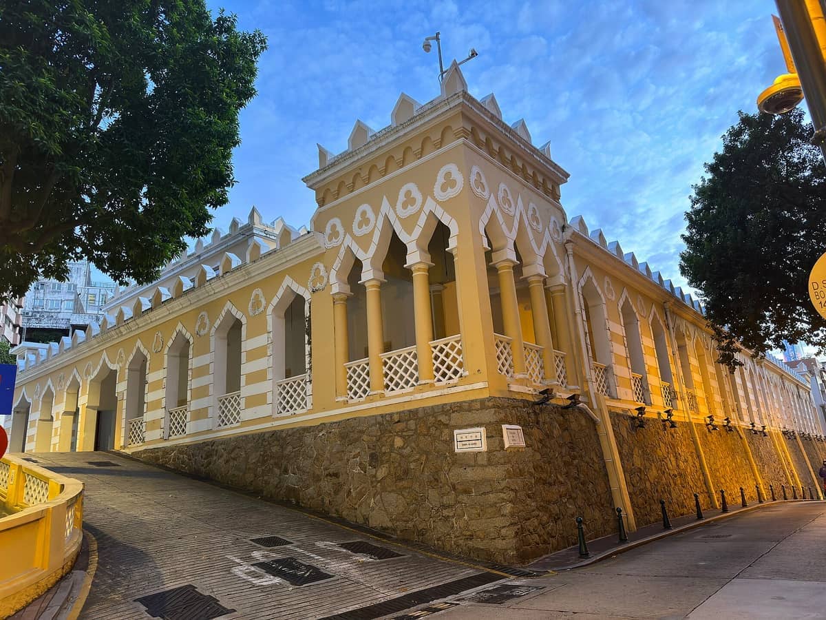 Die Maurischen Kasernen in Macau mit gelb-weißen Bögen im Mogul-Stil, auf einer Steinplattform erhöht, mit Abendbeleuchtung und klarem blauen Himmel.
