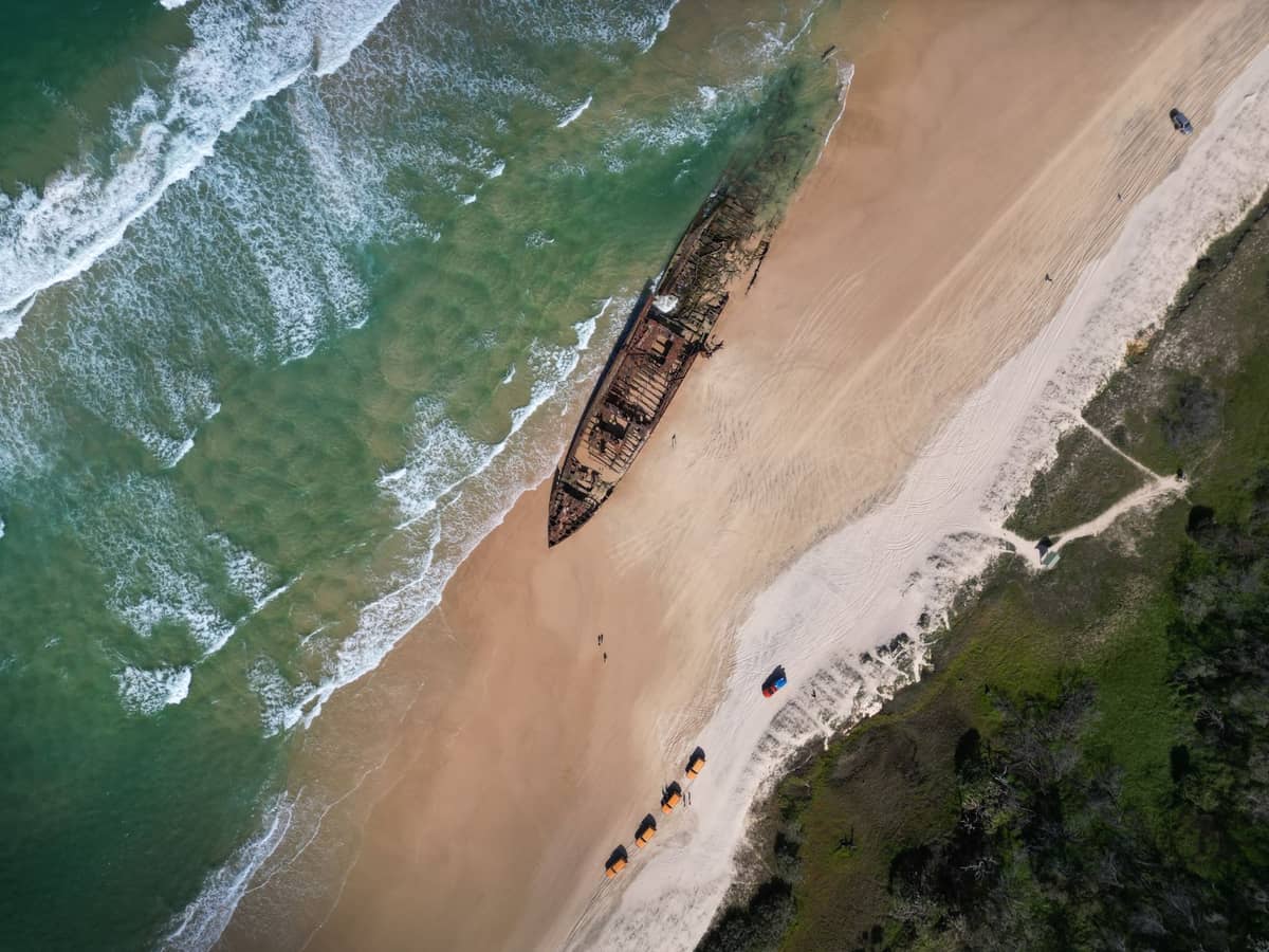 Widok z lotu ptaka na plażę Moreton Island z turkusowymi falami, piaszczystym brzegiem i słynnymi wrakami Tangalooma Wrecks przy linii brzegowej.