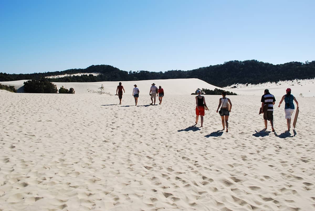 Grupa ludzi spaceruje po jasnych wydmach piaszczystych pod bezchmurnym błękitnym niebem na pustyni Tangalooma na Moreton Island.