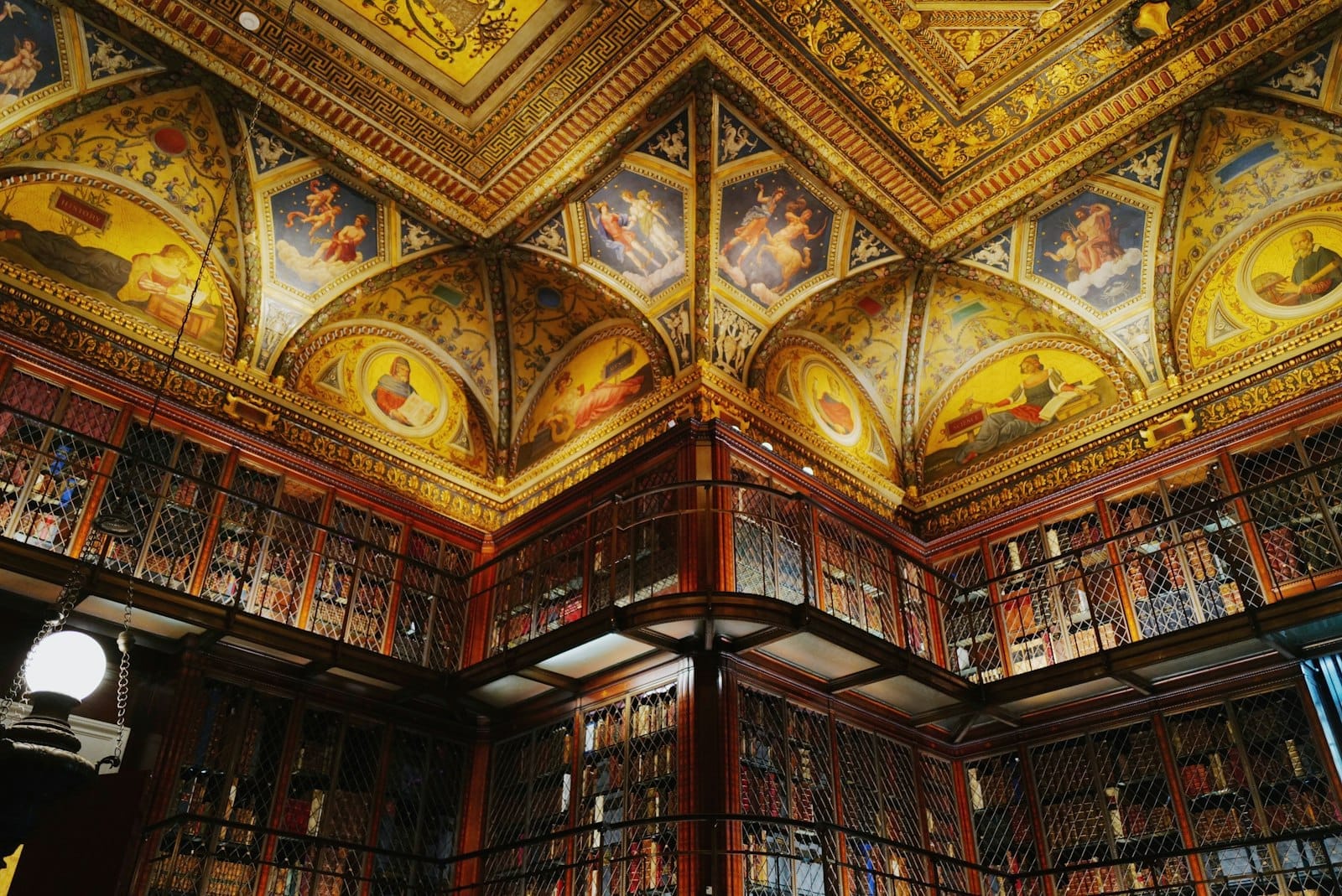 Il soffitto ornato con dettagli dorati e le imponenti librerie della sala di lettura storica della Morgan Library & Museum sotto una luce calda.