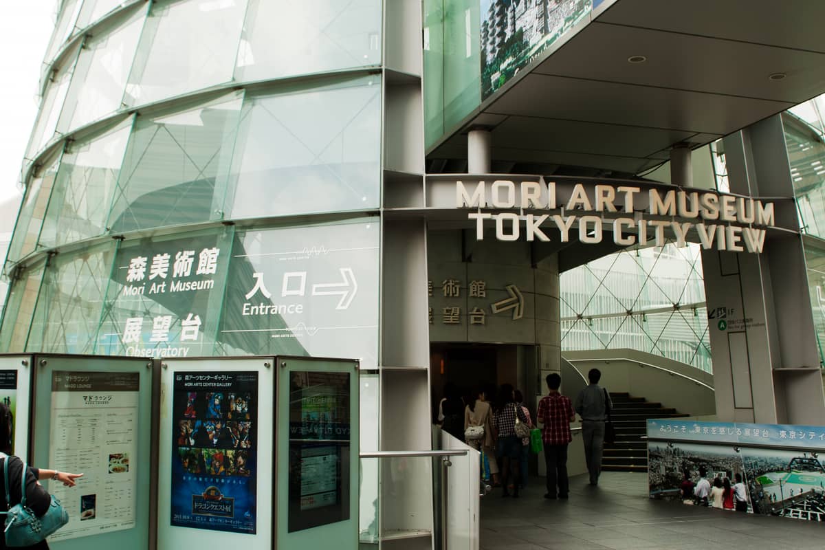 Visitors entering the glass-walled entrance of the Mori Art Museum and Tokyo City View observatory in Roppongi Hills, Tokyo.