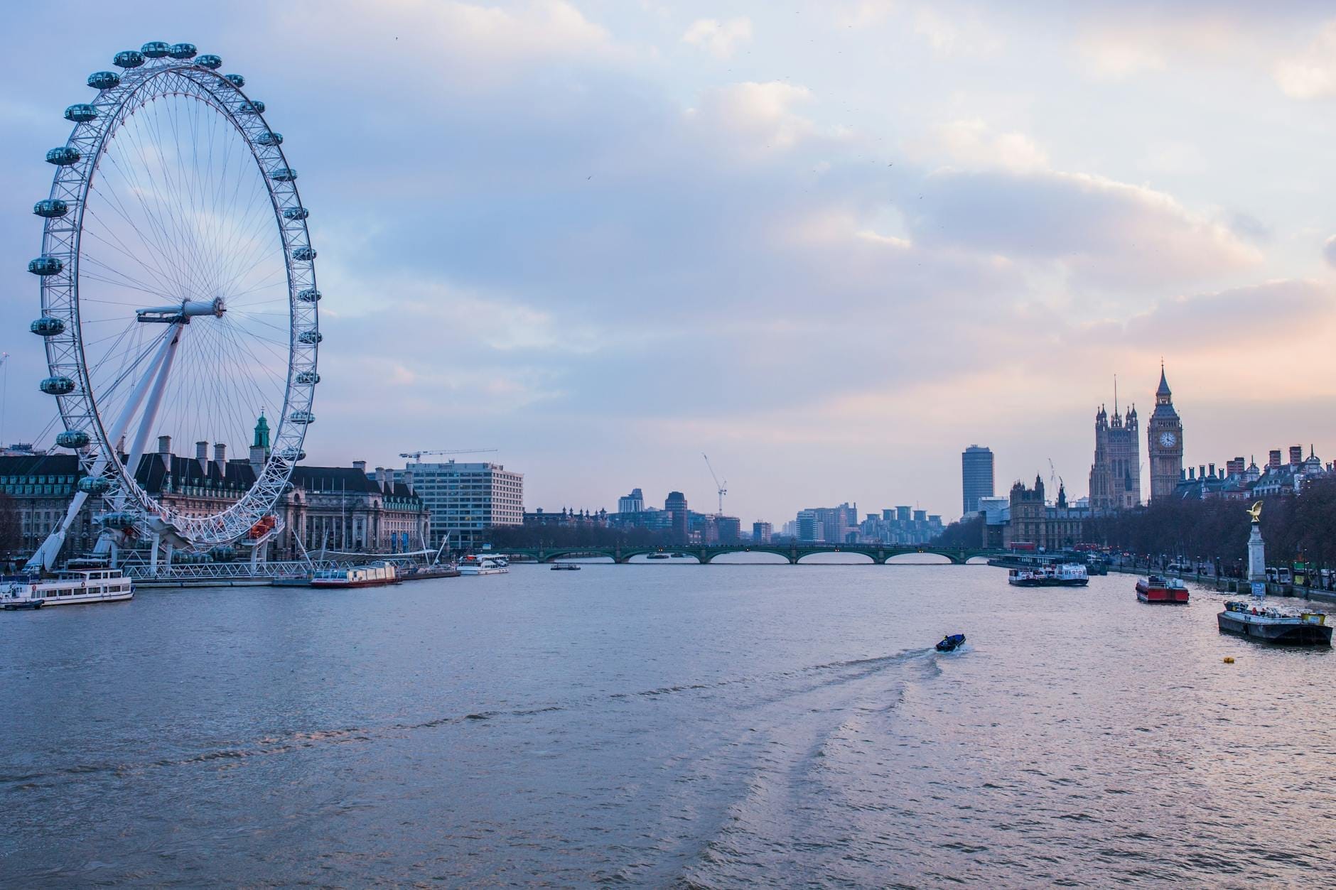 London Eye e o horizonte de Westminster ao pôr do sol com barcos no Tâmisa, pontos icônicos e fotogênicos sob um céu colorido ao entardecer.