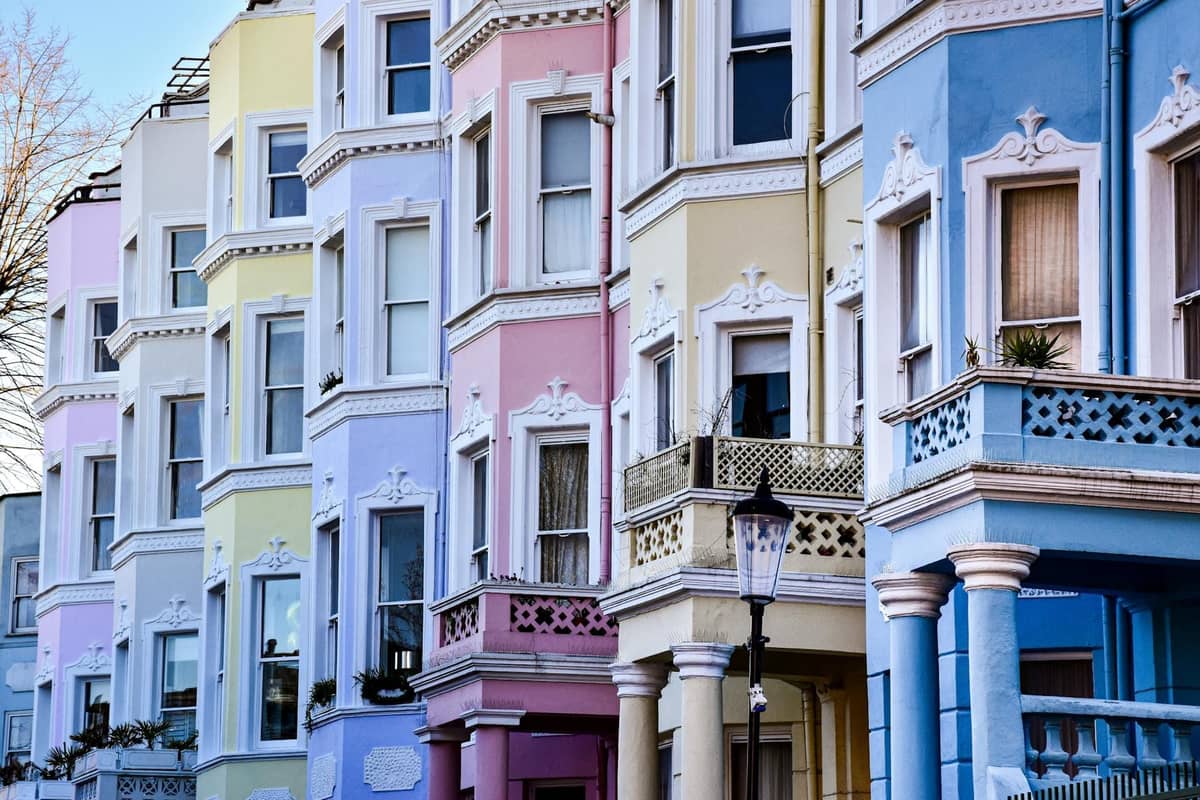 Fileira de casas geminadas em cores pastéis com ornamentados detalhes vitorianos numa rua de Londres, bem iluminadas sob um céu azul.