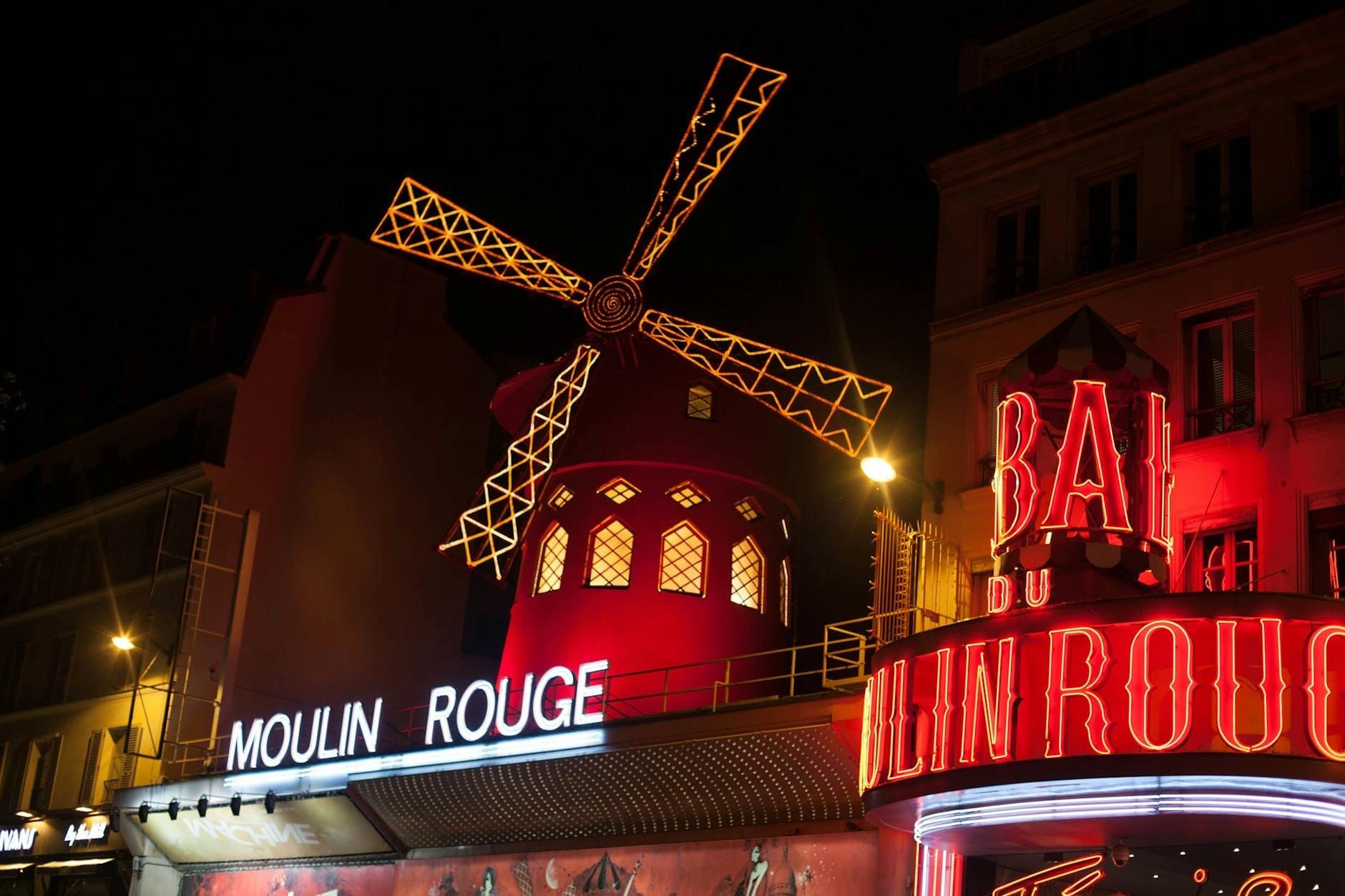 Vista notturna del Moulin Rouge illuminato a Parigi, con il celebre mulino rosso e le insegne al neon vivaci sulla facciata dell'edificio.