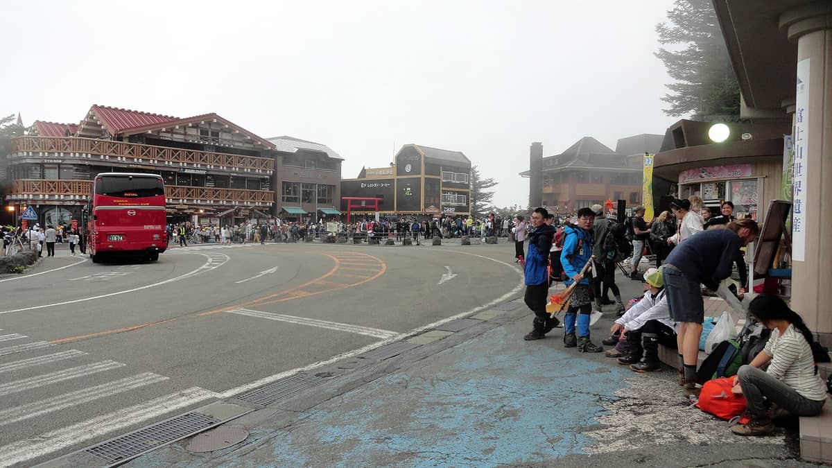 Crowds of hikers and tourists gather at Fuji Subaru Line 5th Station, preparing to climb Mount Fuji, with mountain lodges visible in the background.