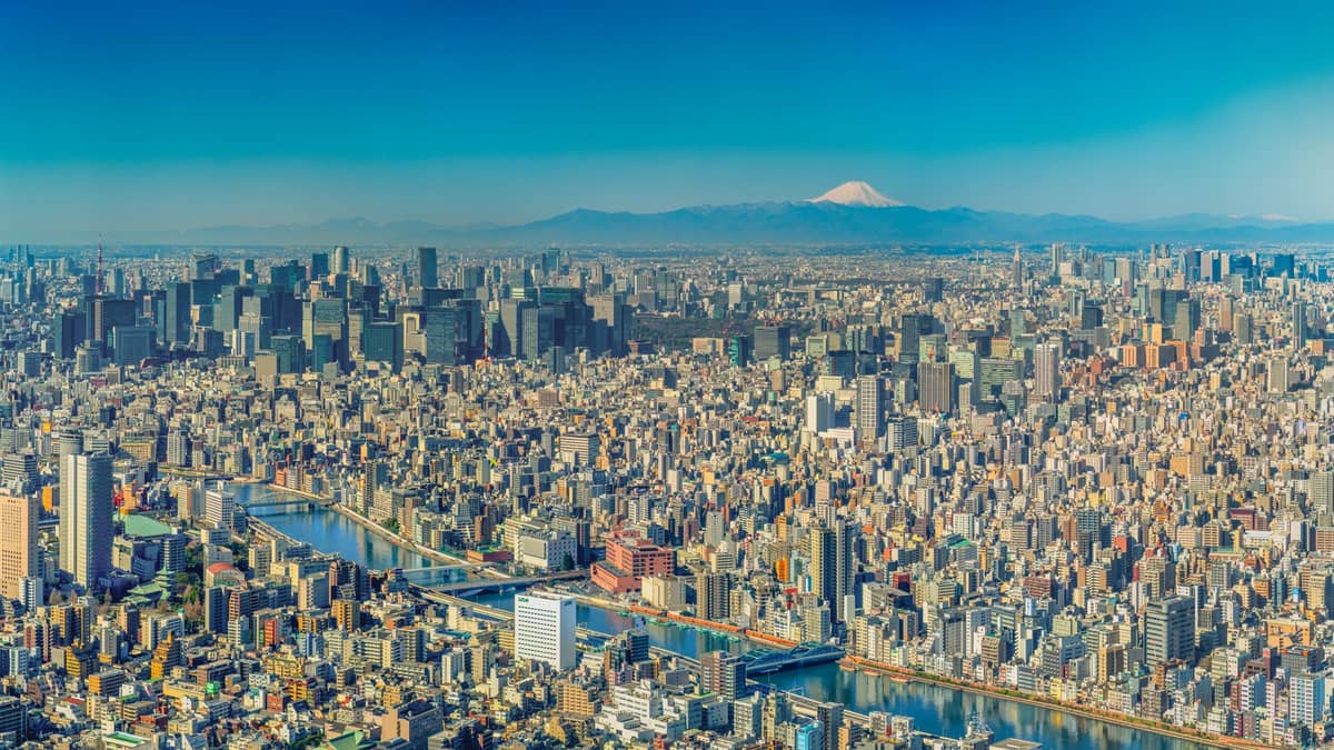 Panoramic view of central Tokyo cityscape with Mount Fuji visible on the distant horizon under a clear blue sky.