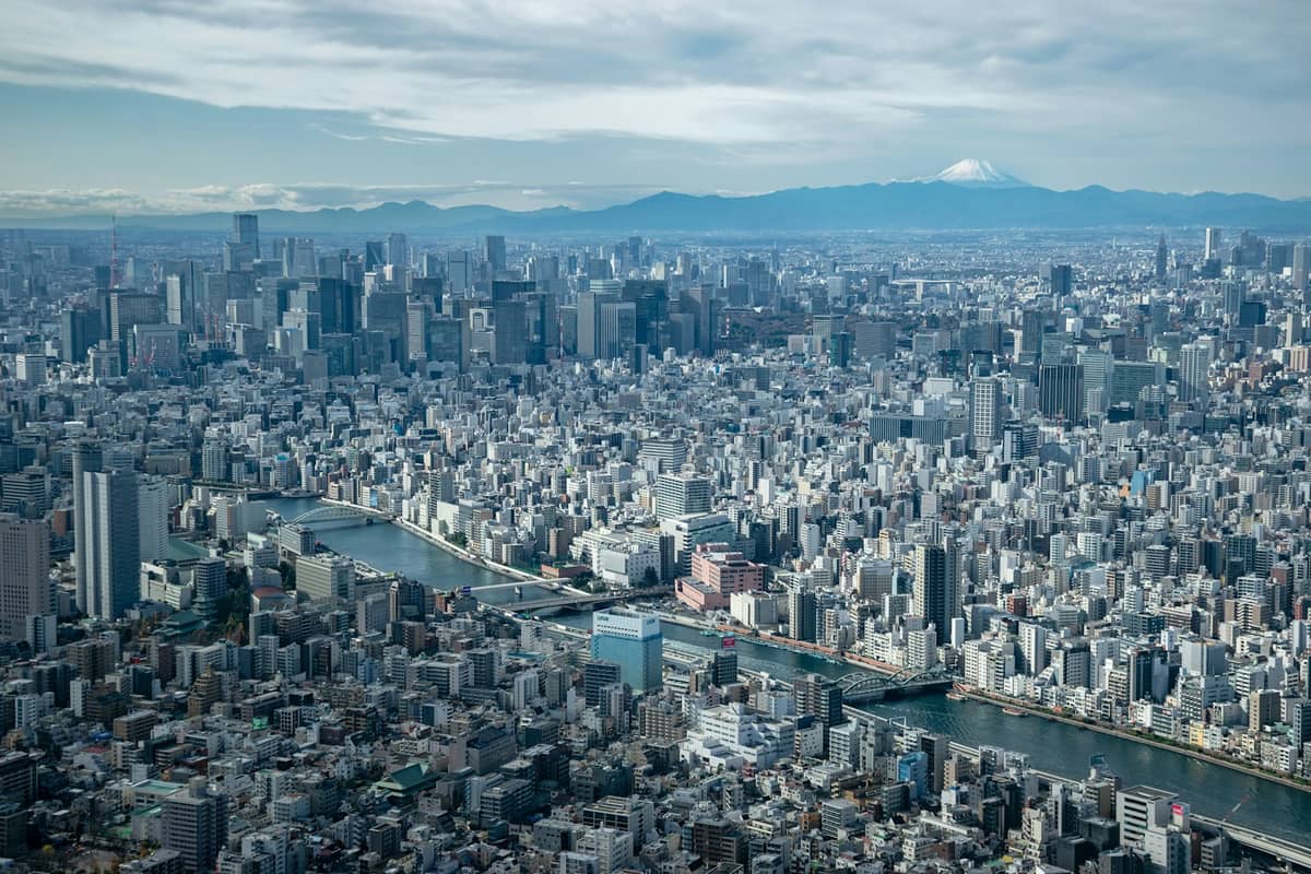 Wide cityscape of Tokyo with Mount Fuji visible in the background on a clear day, showing the city’s dense urban landscape and blue sky.