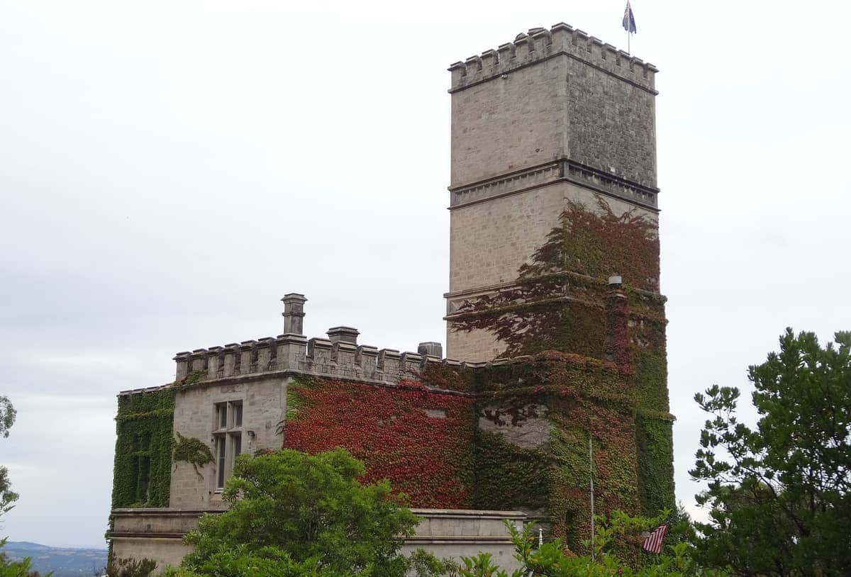 Historic stone tower at Mount Lofty Summit covered in red and green ivy, surrounded by lush greenery under a cloudy sky.