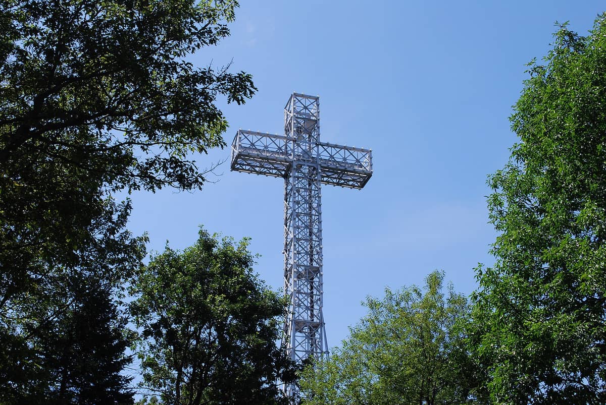 Das große Stahlkreuz auf dem Mont Royal ragt an einem klaren Sommertag über die Baumwipfel – die charakteristische Gitterstruktur vor strahlend blauem Himmel.